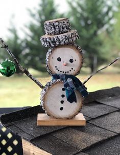 a snowman made out of wood sitting on top of a roof next to a green ornament