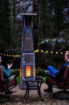 two people sitting in chairs next to an outdoor fire pit with lights on the side