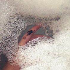 a person laying down in a bathtub with foam on the floor and water droplets all around them