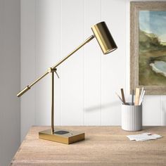 a desk lamp on top of a wooden table next to a painting and pencils