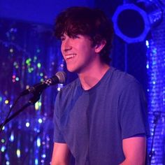 a young man singing into a microphone in front of a blue background with lights on it