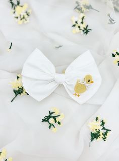 White cotton medium bow with an embordered baby chick.  Length: 5 inches  Finish: Clip or Nylon Headband White Ribbon Bow For Spring, Cute Satin Bow For Spring, Cotton Bow For Spring, Cute White Bow With Ribbon, Cute White Ribbon Bow, Spring Cute Butterfly Knot Bow, Cute Butterfly Knot Bow For Spring, Cute Summer Bow With Ribbon, White Summer Bow For Gifts