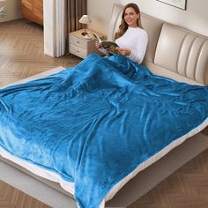 a woman sitting on a bed with a blue blanket over her and reading a book