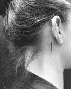 a woman's neck with a small cross tattoo on the back of her left ear