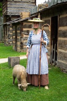 a woman in an old fashioned dress and straw hat is standing next to a sheep