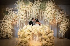 a bride and groom kissing in front of a floral arch with candles on it at their wedding reception