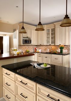 a kitchen with marble counter tops and white cabinets, along with two hanging lights over the island