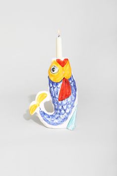 a ceramic candle holder with a fish design on the front and side, holding a lit candle