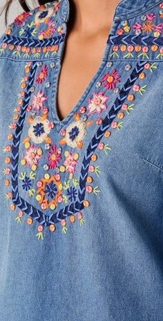 a woman wearing a denim shirt with colorful embroidered flowers on the chest and shoulder, close up