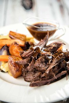 a white plate topped with meat and vegetables next to a dipping sauce on top of it