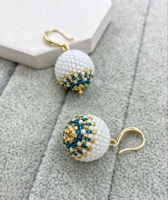 two white and blue beaded earrings sitting on top of a gray blanket next to a box