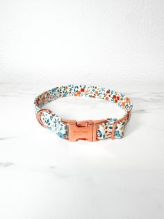 a dog collar with flowers on it and a pink metal buckle in the center, sitting on a marble surface