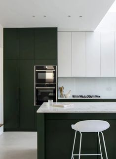 a kitchen with green cabinets and white stools in front of an island countertop