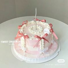 a pink and white cake on a table with ribbon around the edges, topped with a single candle