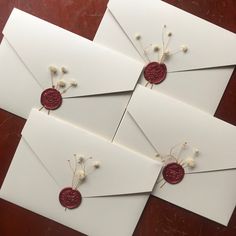 four white envelopes with red wax stamping and flower decorations on them, sitting on a wooden table