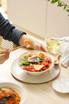 a person eating food at a table with chopsticks in their hand and wine glass next to it