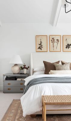 a white bed sitting under two framed pictures on the wall above it's headboard