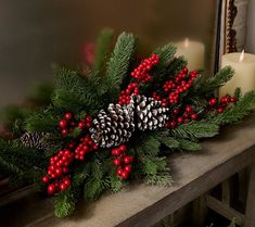 a candle and some pine cones are on a mantle with red berries, holly and candlesticks