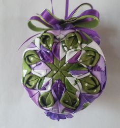 an ornament made out of fabric with green leaves and purple ribbons on it