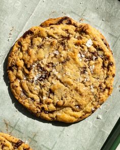 two chocolate chip cookies sitting on top of a piece of parchment paper next to each other