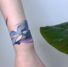 a woman's arm with a blue and purple flower tattoo on the left wrist