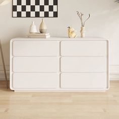 a white dresser with two vases on top and a black and white painting above it