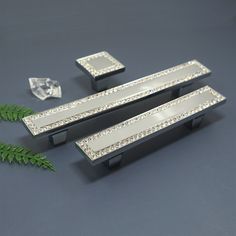 two black and silver drawer pulls with diamonds on them next to a green fern leaf