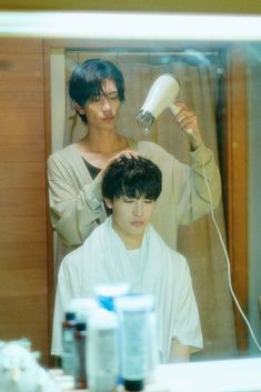 two people blow drying their hair in front of a mirror