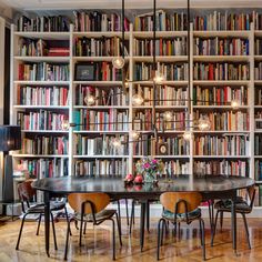 a dining room table surrounded by bookshelves with chairs and lamps on each side