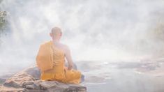 a man sitting on top of a rock next to a body of water with steam coming out of it