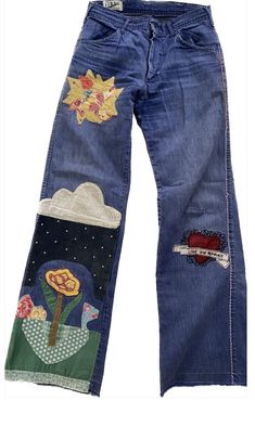 a pair of blue jeans with patches and flowers on the side, sitting against a white background