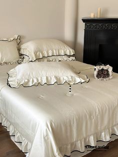 a bed with white sheets and pillows on it next to a black fireplace mantel