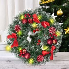 a christmas wreath with red and green decorations on top of a wooden table next to a christmas tree