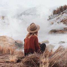 a woman sitting on top of a dry grass covered field next to a body of water