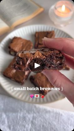 a person holding a piece of chocolate brownie on a plate with candles in the background