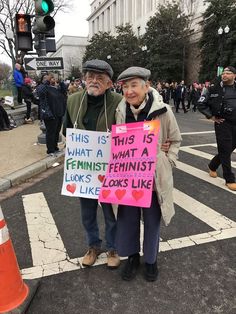 two people standing in the street holding signs that read this is what a feminist looks like