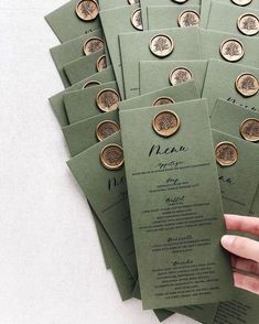 a hand is holding a green menu card with gold buttons on it and several other cards are in the background