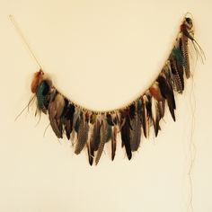 a necklace with feathers hanging from it's side on a white wall next to a string