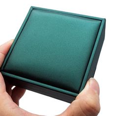 a hand holding a small green box in it's left hand, with the lid partially closed