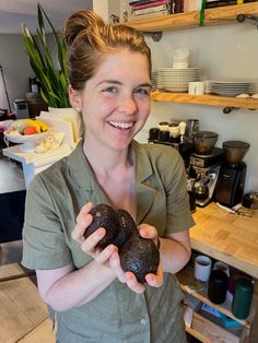 a woman holding two chocolate donuts in her hands while standing next to a counter