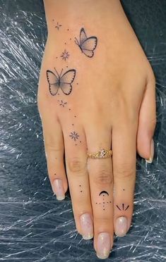 a woman's hand with tattoos on it and two butterflies flying over her finger