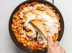 a person stirring food in a skillet with a wooden spoon