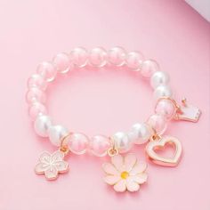 a pink bracelet with a flower and heart charm on it, sitting on a pink surface