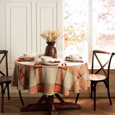 the table is set for two with plates and cups on it, along with an orange plaid tablecloth