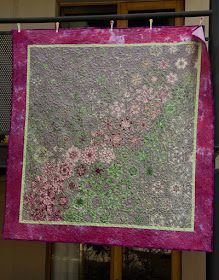 a purple and green quilt hanging from a clothes line