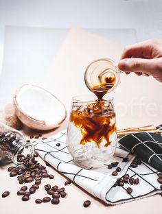 a person pouring coffee into a glass on top of a table next to some beans