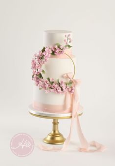 a wedding cake decorated with pink flowers and ribbons on a gold plated platter