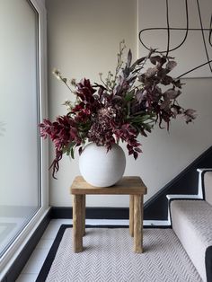 a vase filled with flowers sitting on top of a wooden table next to a stair case