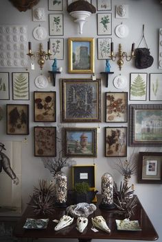 there are many framed pictures on the wall above this dining room table, along with vases and other decorative items