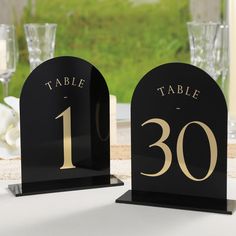 two black and gold table numbers sitting on top of a table next to wine glasses